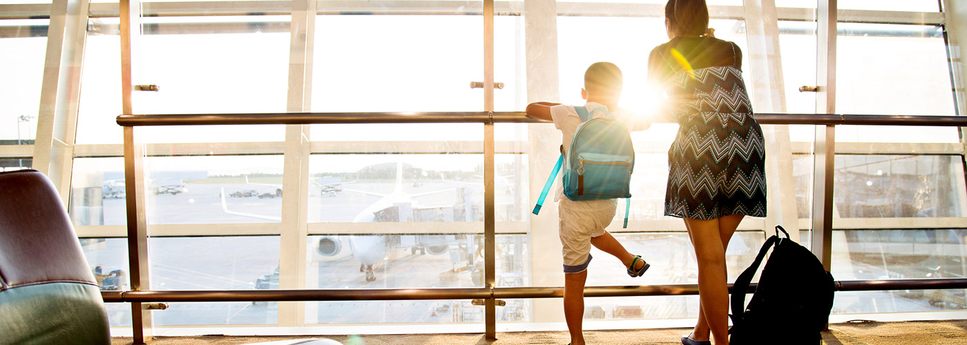 Madre e Hijo en un aeropuerto viendo por una ventana, esperando su vuelo por la tarde.